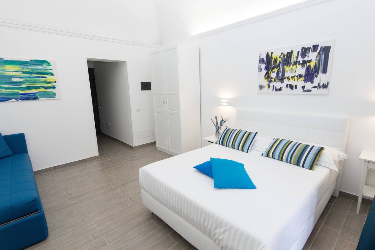 Una moderna camera d'albergo con un letto grande, un divano blu e opere d'arte astratte alle pareti.
