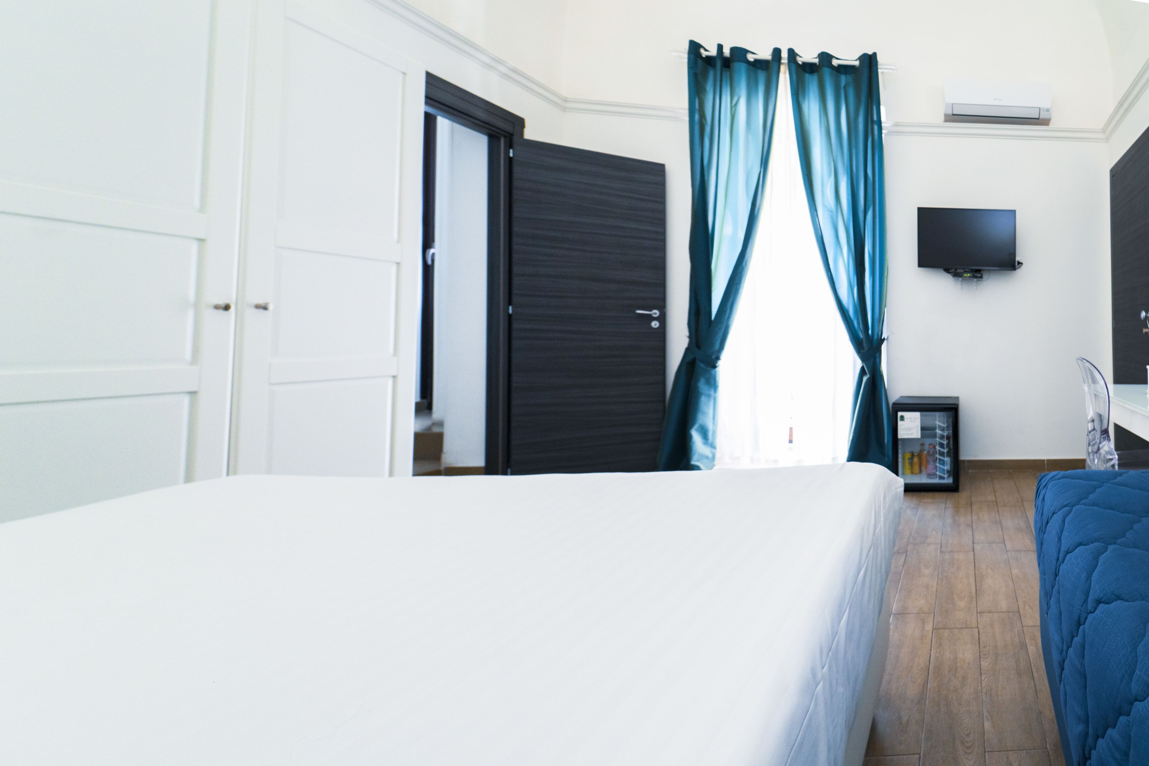 A hotel room with a bed, a television, a minibar, and a door.