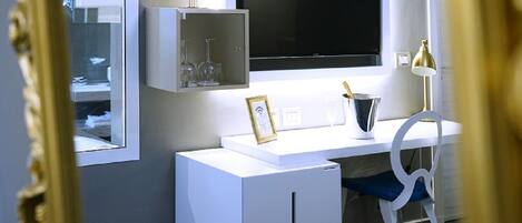 A modern room with a white desk, a flat-screen TV, a small cabinet with wine glasses, and a chair.