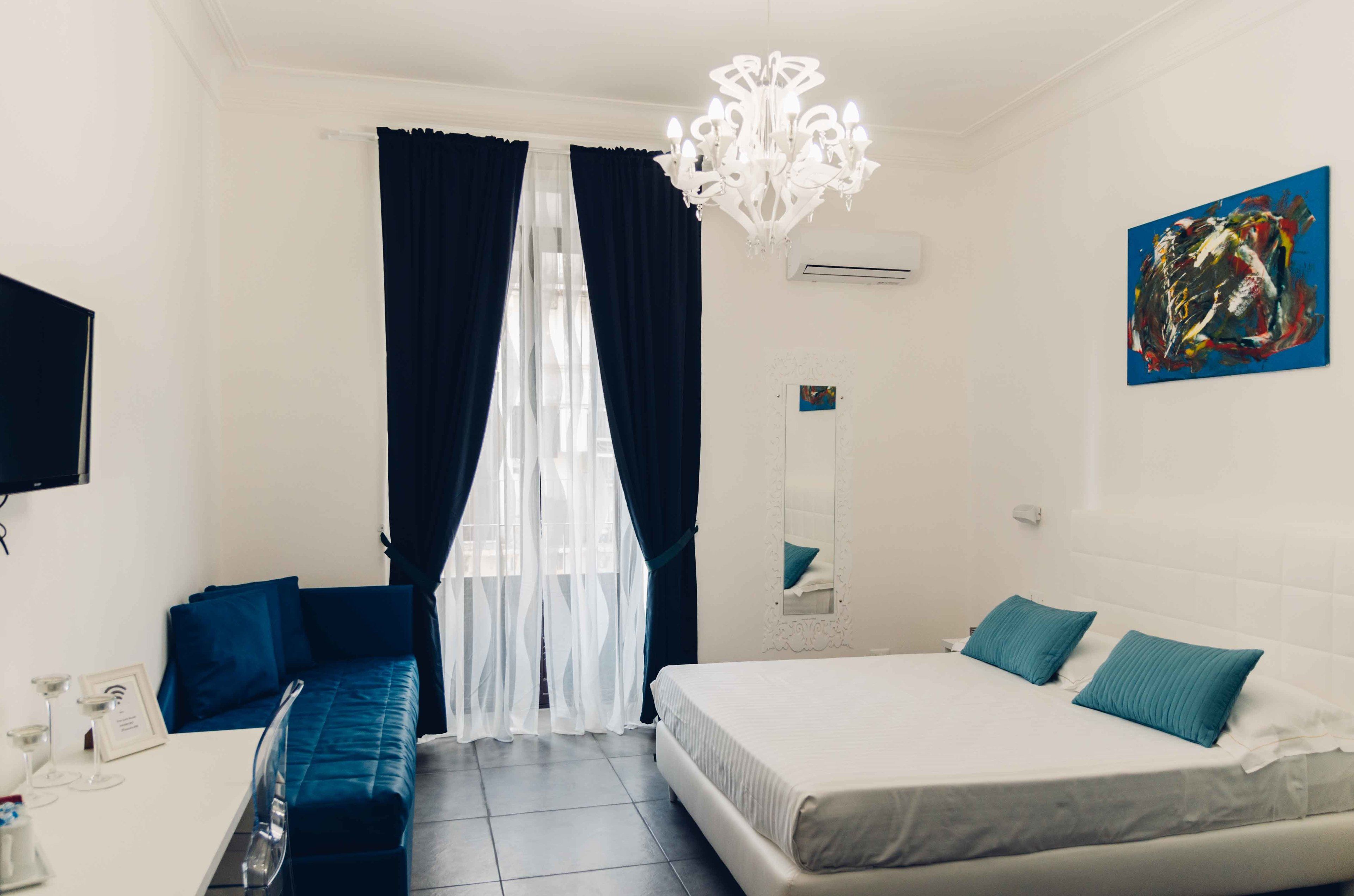 A hotel room with a bed, a sofa, a chandelier, a painting, and a television.