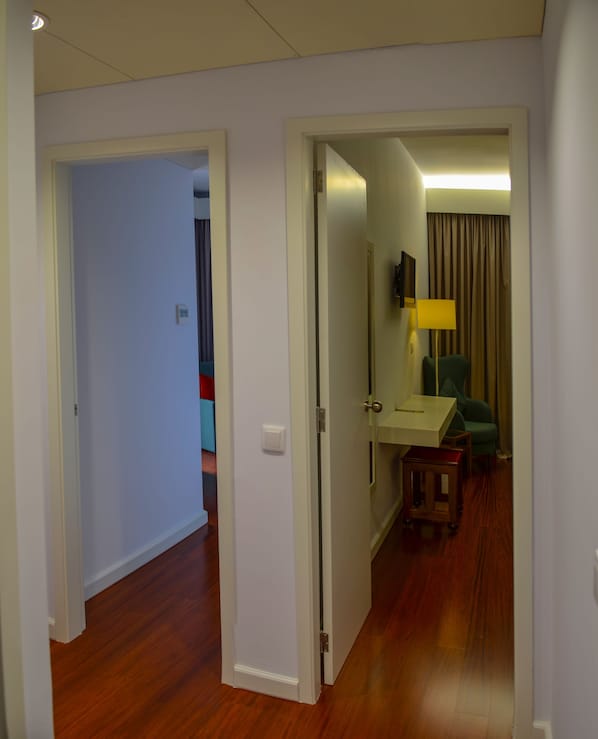 A hotel room with a wooden floor, a bed, a bedside table, a lamp, and a view of the hallway. - Hotel São Bento da Porta Aberta & Spa (Terras de Bouro)