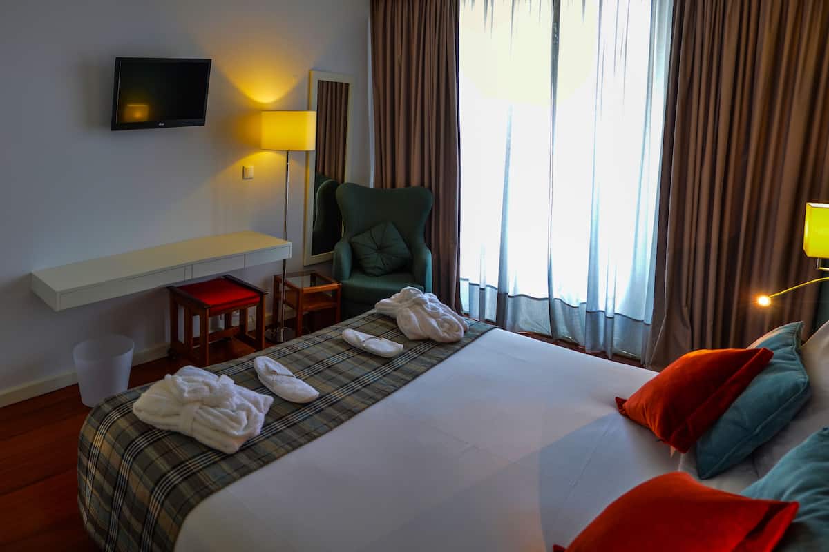 A hotel room with a bed, a desk, a chair, a TV, and a window with curtains.