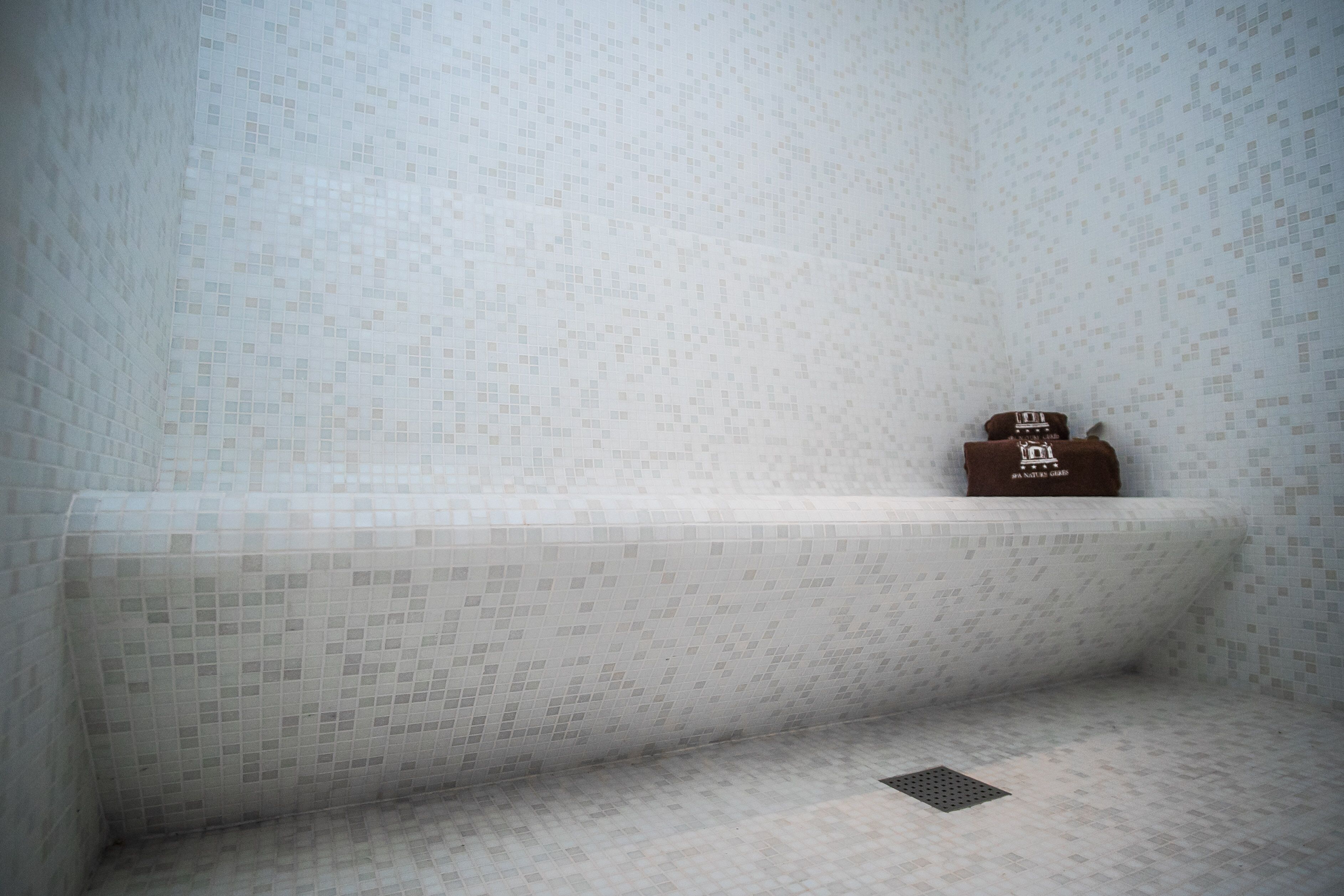 Un baño con suelo y paredes de azulejos, un banco y un perchero con una toalla.