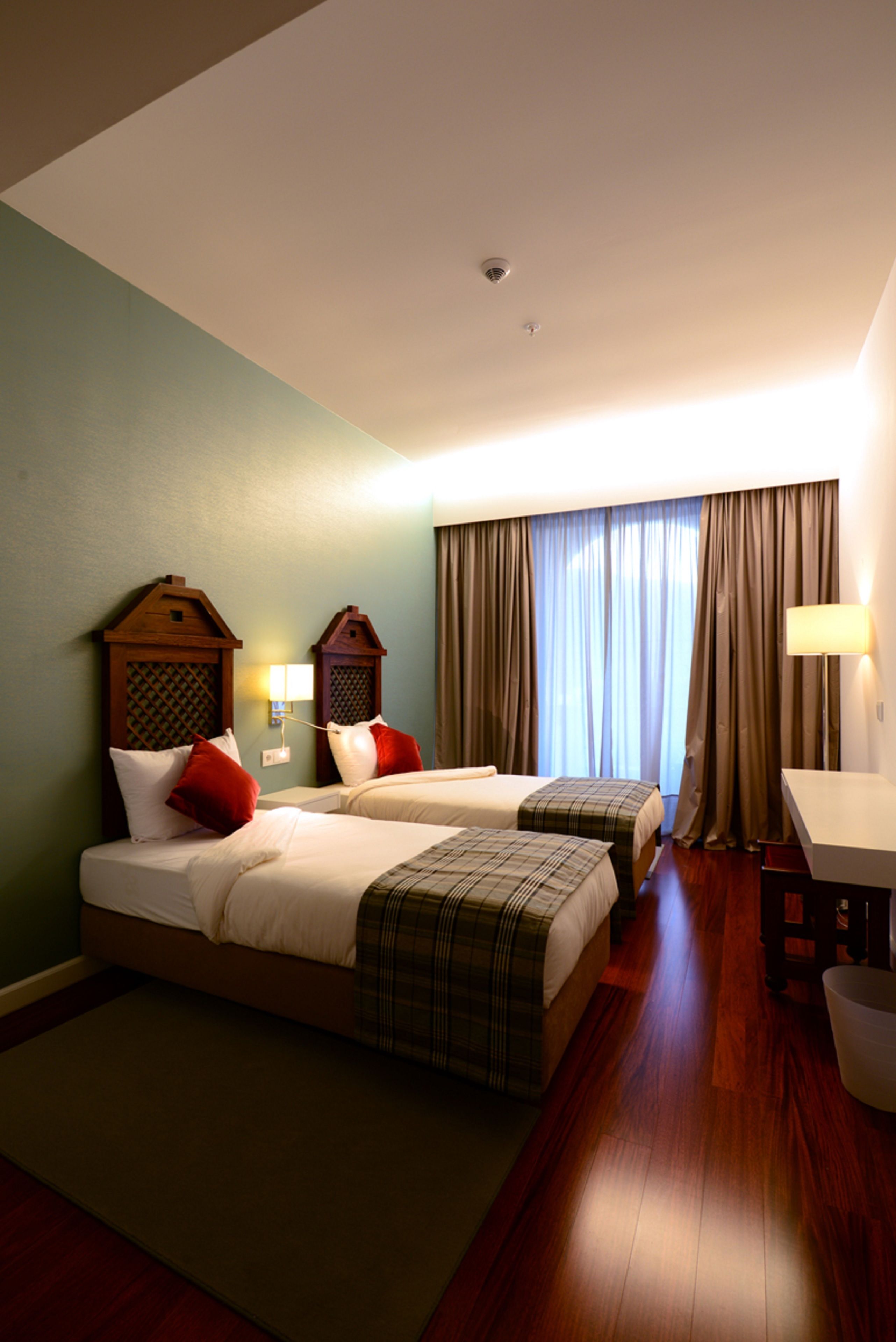 Une chambre d’hôtel avec deux lits, un bureau, une chaise et une fenêtre avec des rideaux.