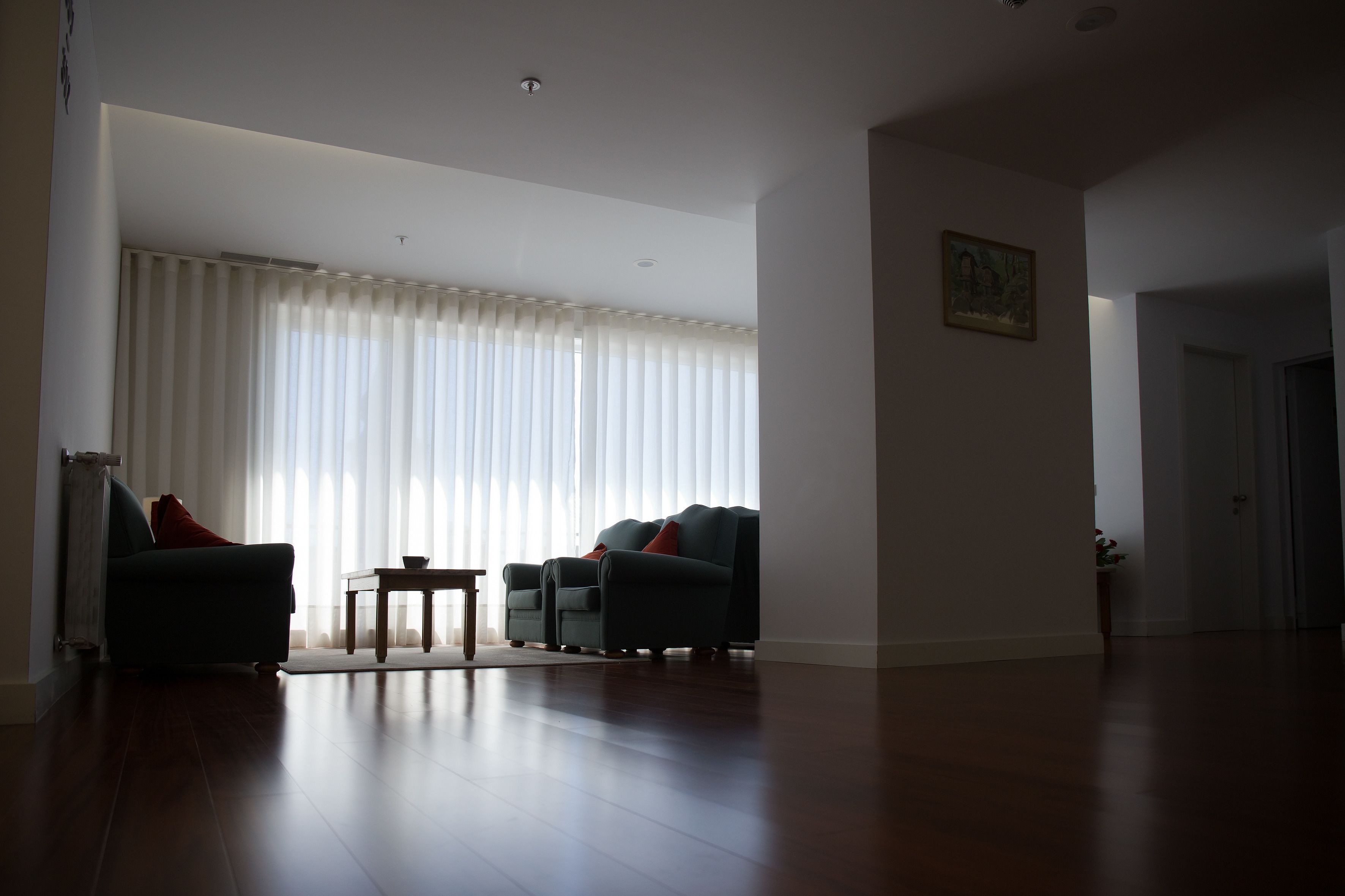 Een ruime woonkamer met een groot raam, twee banken, een klein tafeltje en een deur naar een andere kamer.