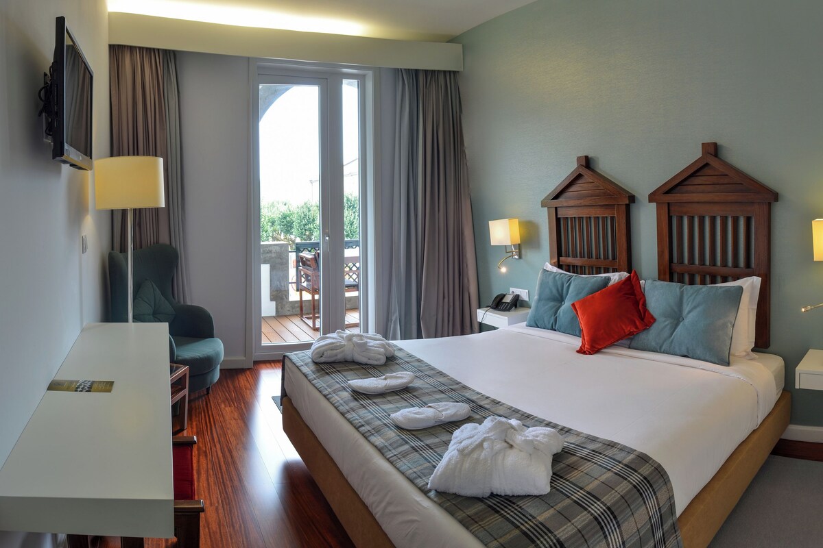 A hotel room with a bed, a desk, a chair, a TV, and a balcony.