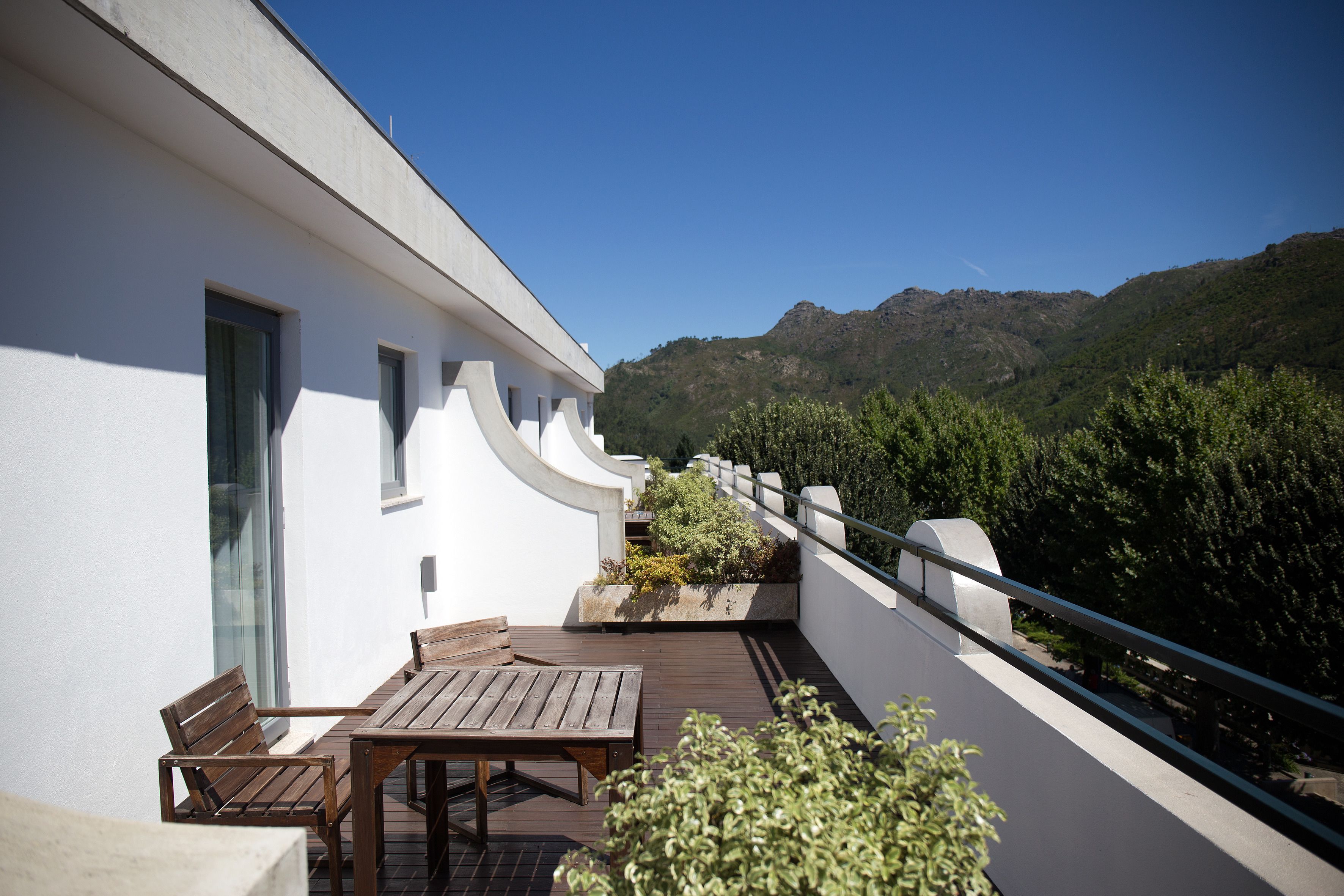 Ein Balkon mit Holztisch und -stühlen mit Blick auf eine gebirgige Landschaft.