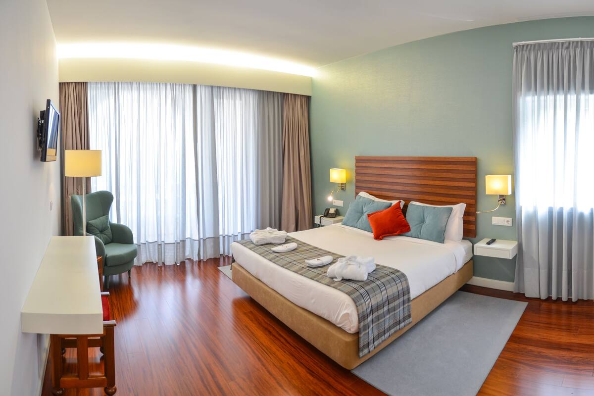 A hotel room with a large bed, a desk, a chair, and a TV.