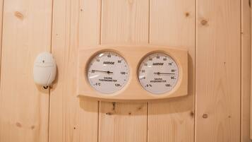 A wooden wall with two circular devices labeled "HARVIA SAUNA THERMOMETER" and "HARVIA SAUNA HYGIOMETER" mounted on it.