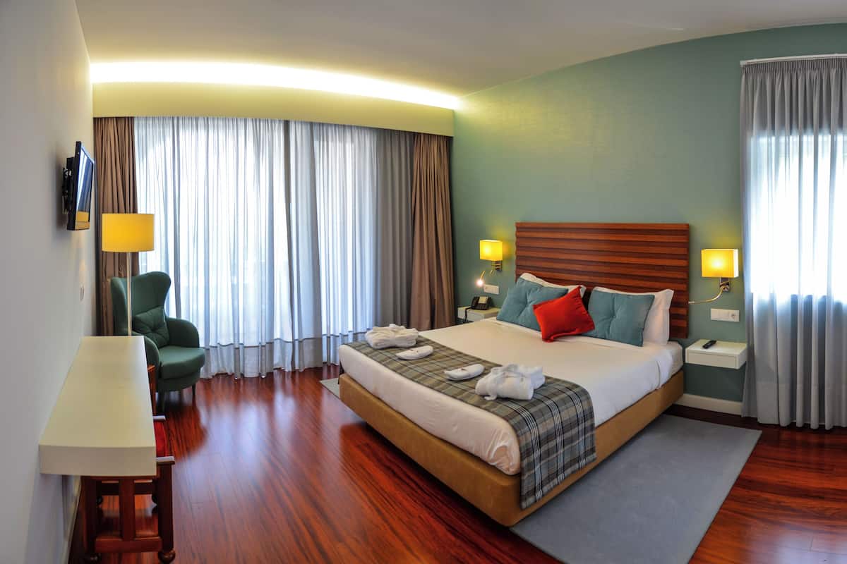 A hotel room with a large bed, a desk, a chair, a TV, and a window with curtains.
