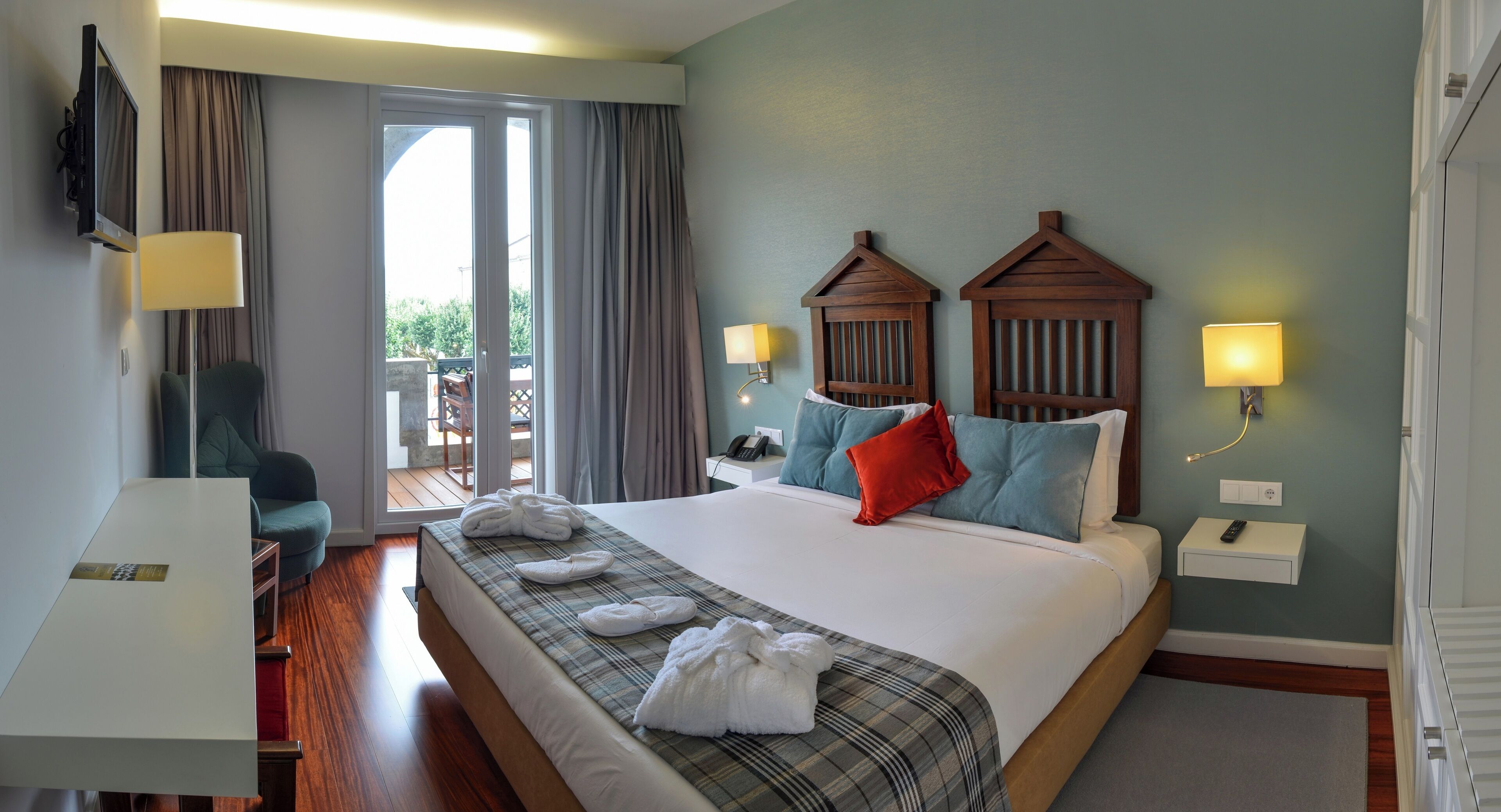 A hotel room with a bed, a desk, a chair, a TV, and a balcony.