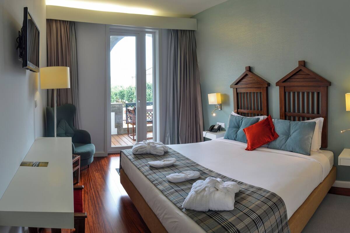A hotel room with a bed, a desk, a chair, a TV, and a balcony.