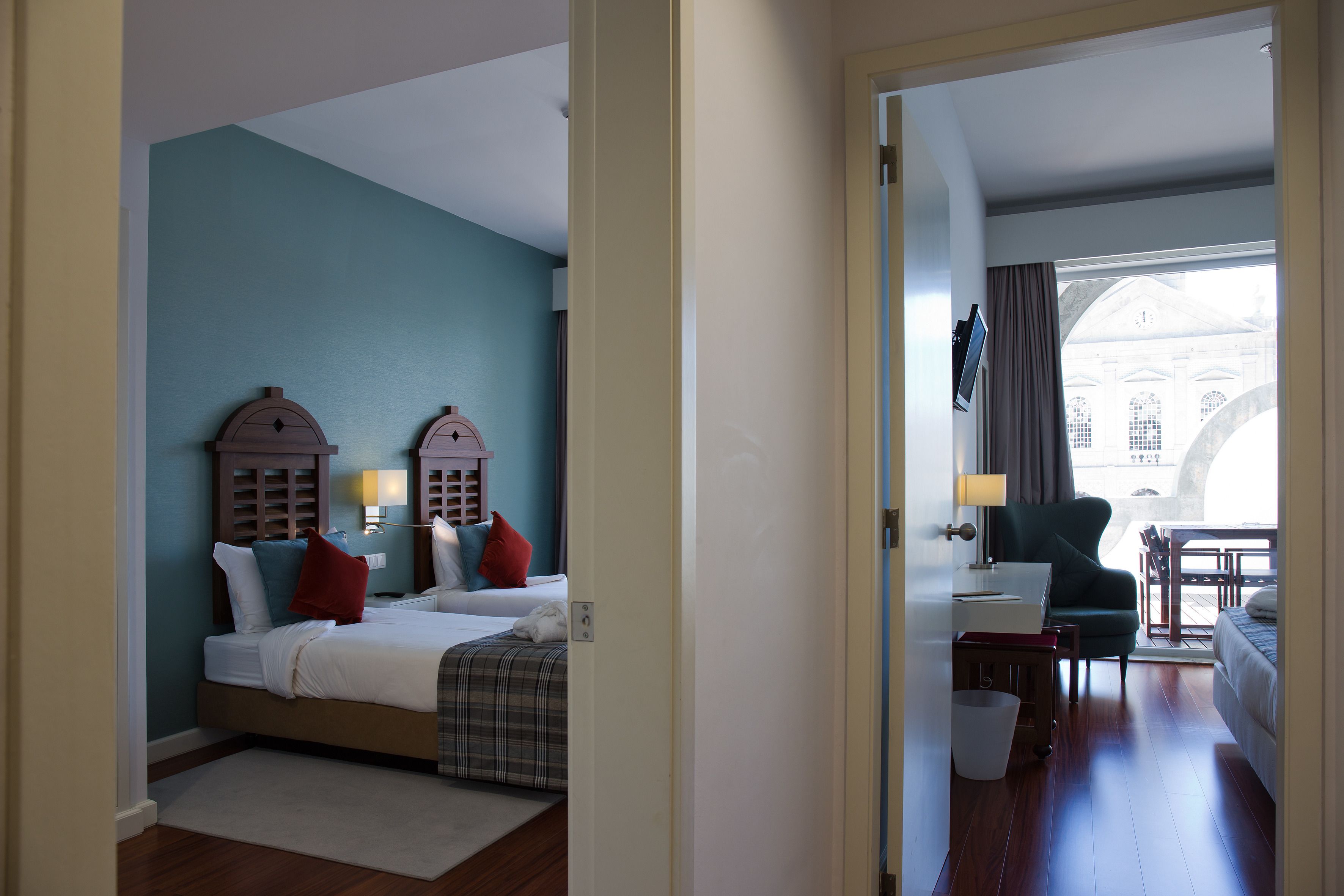 A hotel room with a bed, a desk, a chair, and a view of a building through a window.