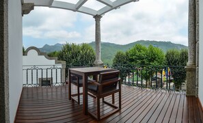 A wooden deck with a table and chairs, a white wall with a window, and a view of green hills and a blue sky. - Hotel São Bento da Porta Aberta & Spa (Terras de Bouro)