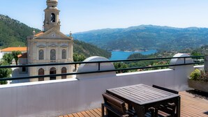 A terrace with a wooden table and benches, overlooking a church with a bell tower and a view of a lake and mountains. - Hotel São Bento da Porta Aberta & Spa (Terras de Bouro)