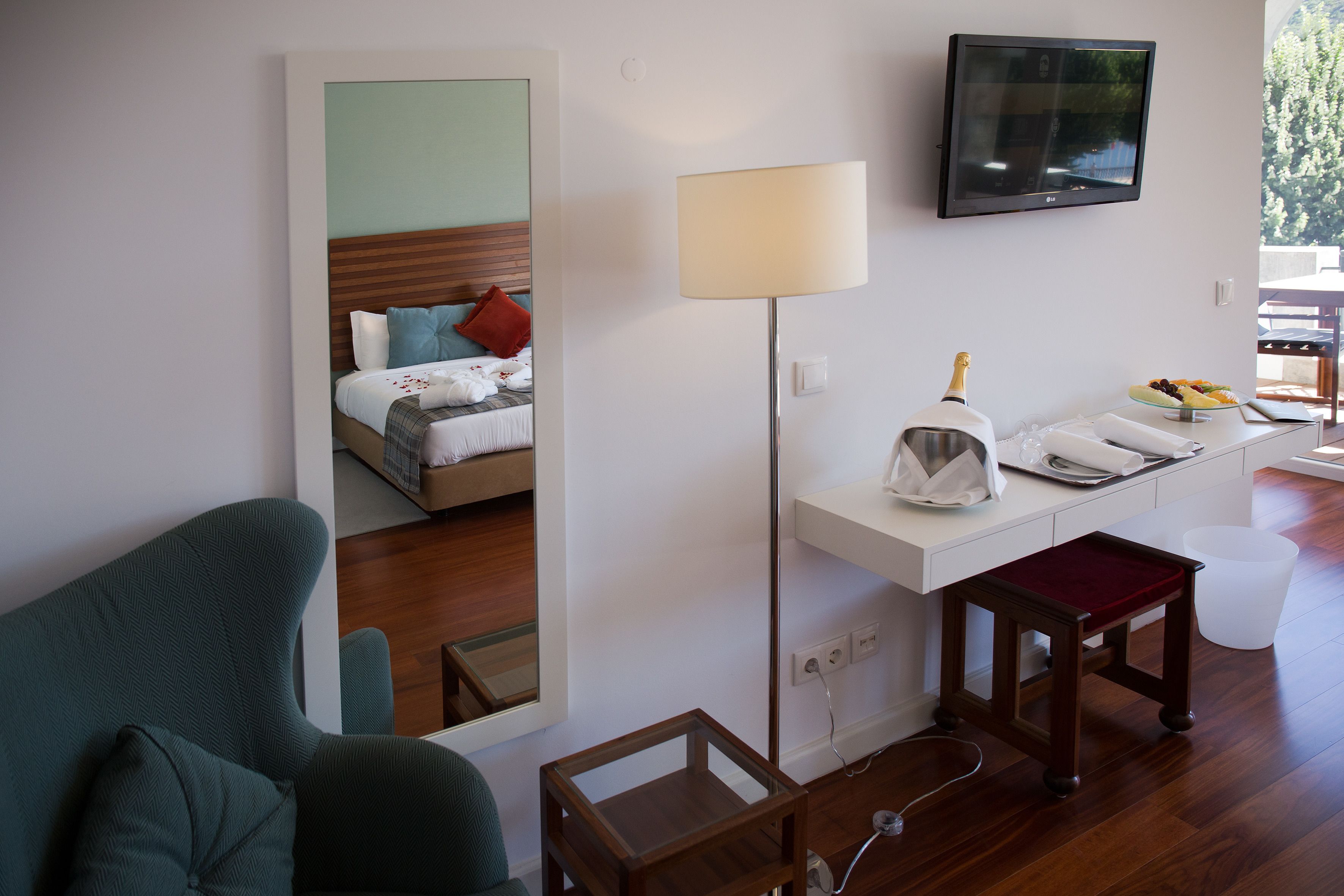Habitación de hotel con cama, escritorio con lámpara, televisor y vistas al exterior.