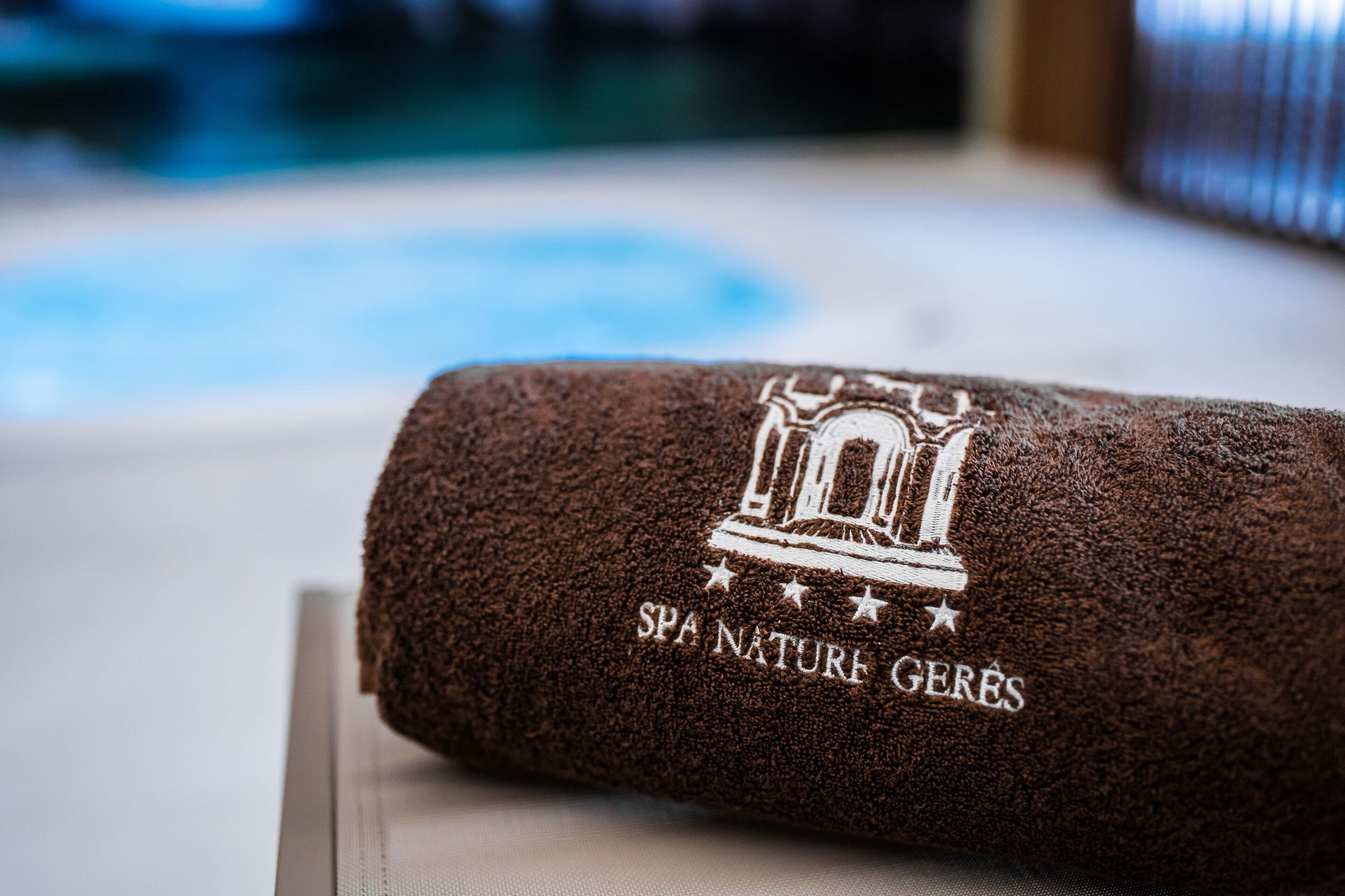 En ihopvikt, brun handduk med en logotyp för ett spa och texten ”SPA NATURE GERES” på en träyta.