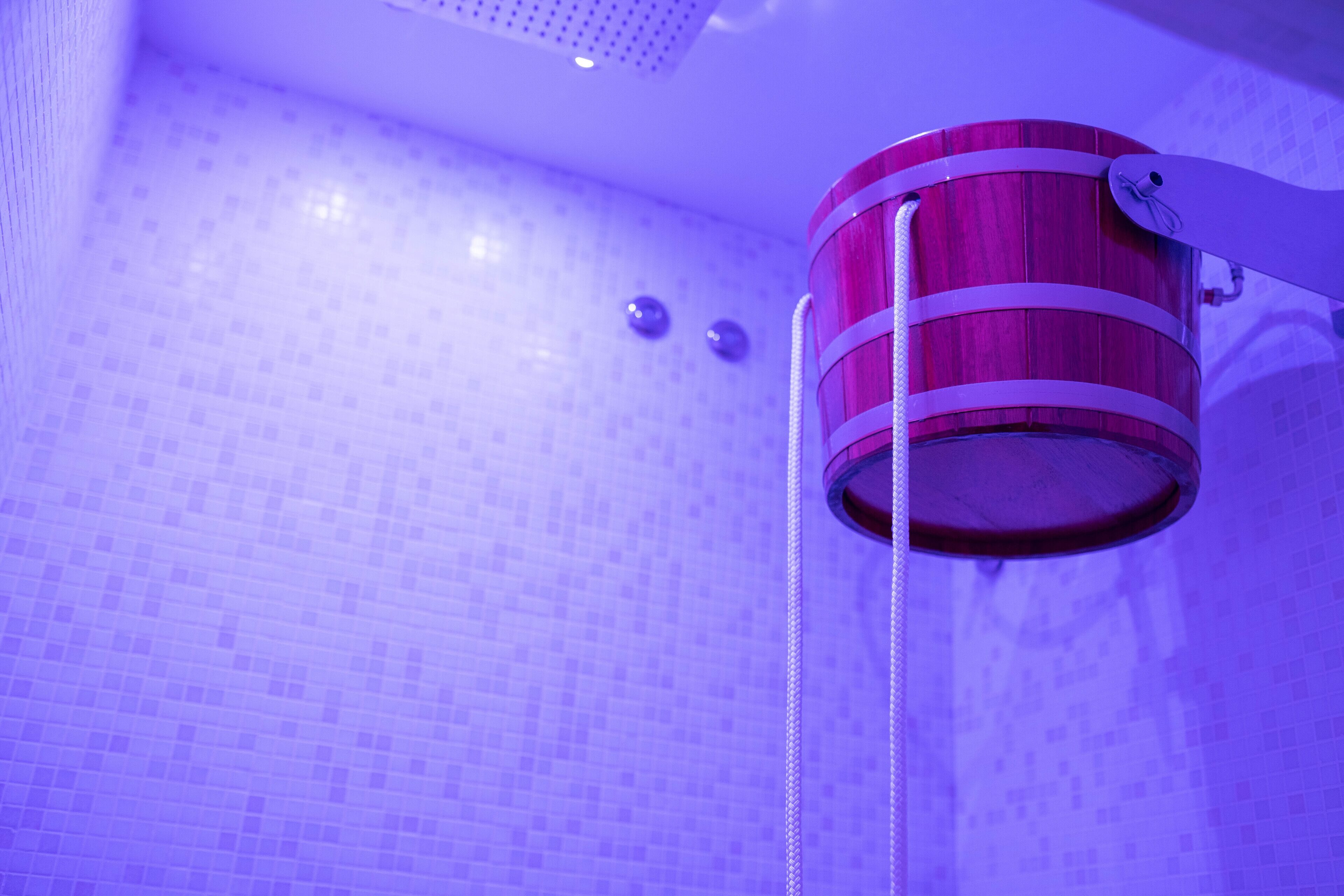 Un baño con ducha de cubo de madera, paredes con azulejos e iluminación en el techo.