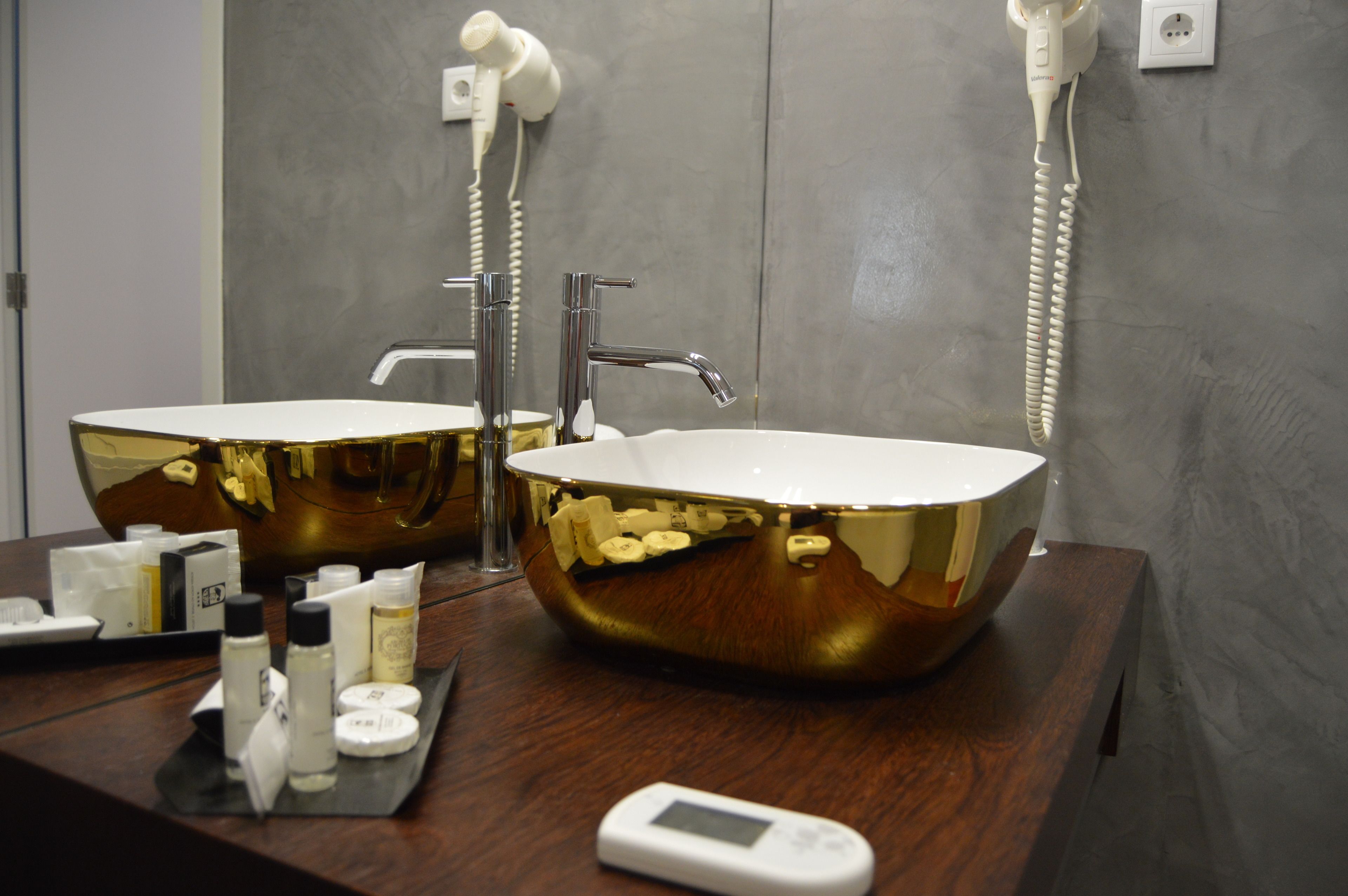 Un baño con dos lavamanos con acabados dorados, un secador de pelo y artículos de aseo en la encimera.