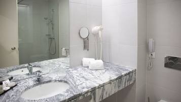 Un baño con lavamanos de mármol, espejo de mano y secador de pelo en la pared.