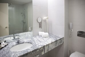 A bathroom with a marble sink, a handheld mirror, and a hairdryer on the wall. - Hotel São Bento da Porta Aberta & Spa (Terras de Bouro)