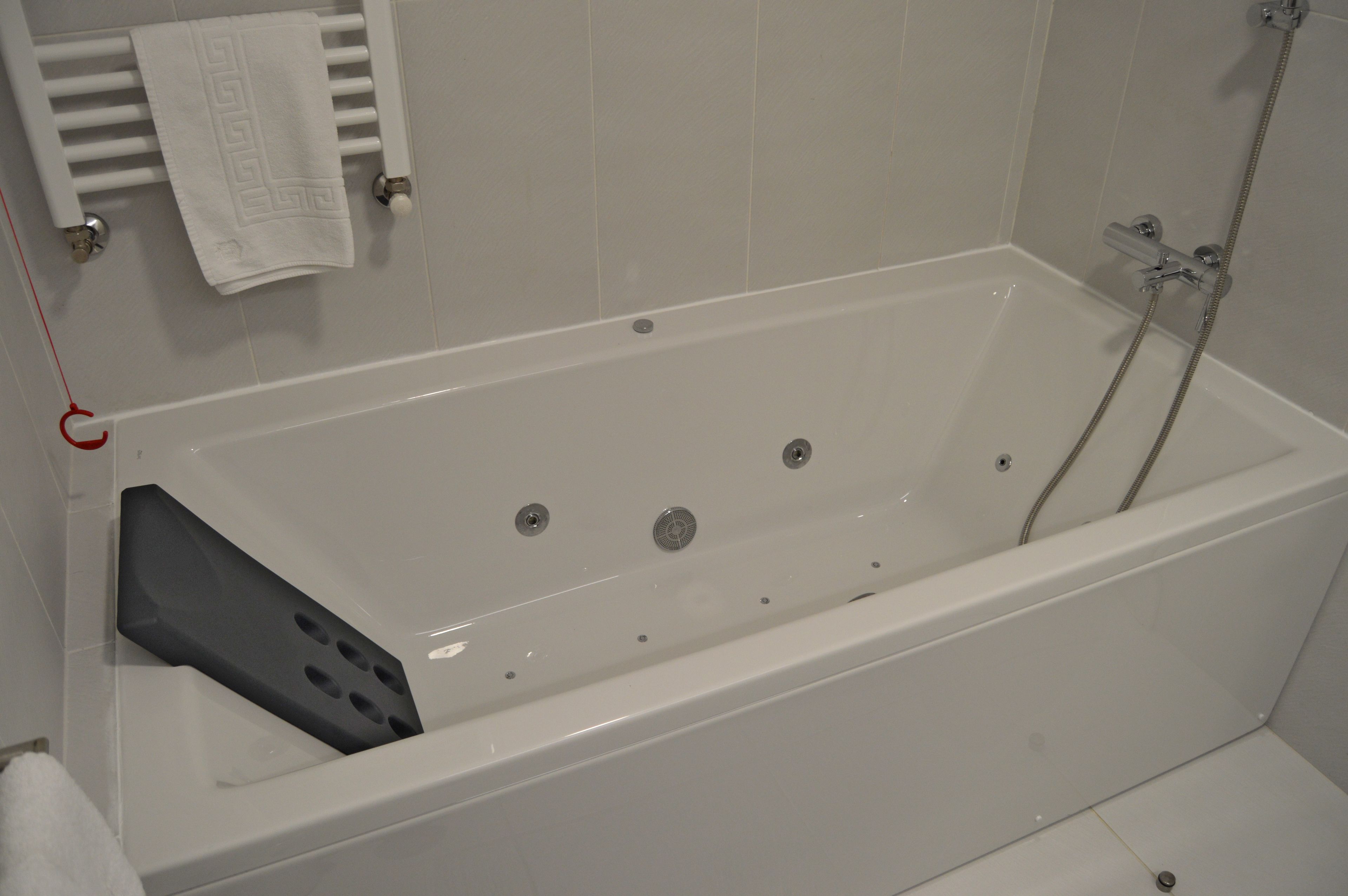 Une baignoire blanche dotée d’un siège intégré, d’une pomme de douche et d’un porte-serviettes avec une serviette.