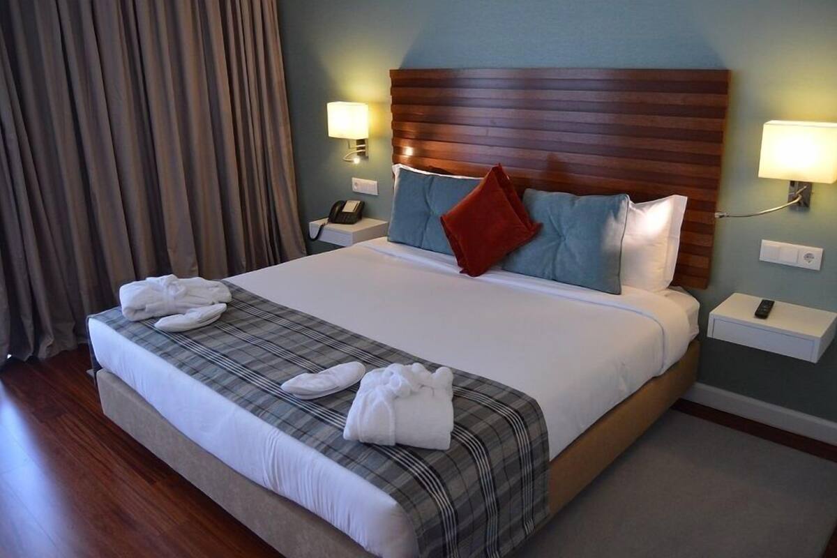 A hotel room with a large bed, two bedside tables, a nightstand, and a lamp.