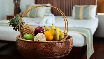 A wicker fruit basket with pineapple, apple, banana, and lime on a bed with white bedding and wooden headboard.