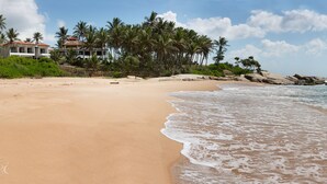 A beach with a sandy shore, palm trees, and a building with a red roof.