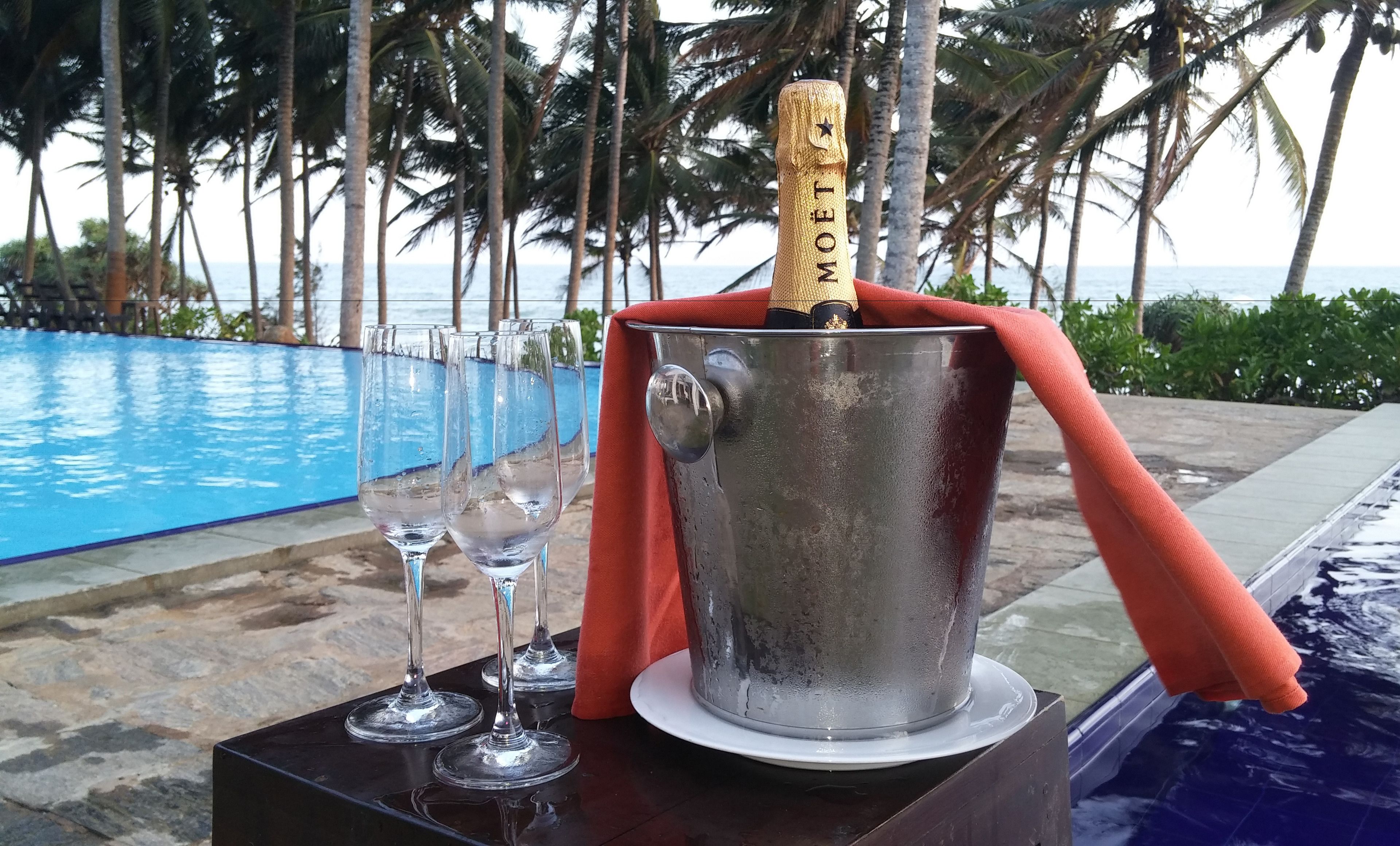 Un balde de champán con un corcho, copas y una toalla junto a una piscina.