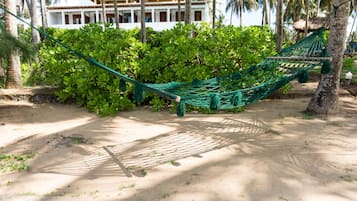 A hammock tied between trees in a sandy area with a building in the background.