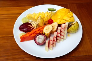 A plate of assorted fruits including mango, banana, apple, and grapes.