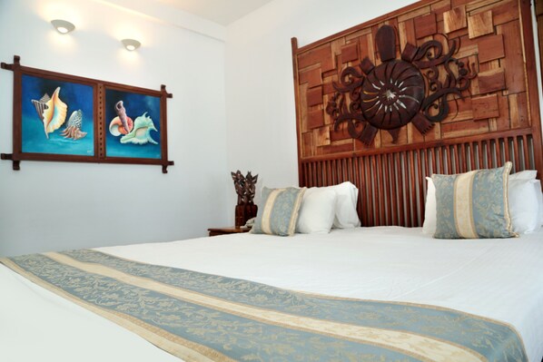 A neatly made bed with a blue and gold bedspread, a wooden headboard with a decorative panel, and two wall-mounted paintings of sea creatures. - Turtle Bay (Tangalle)