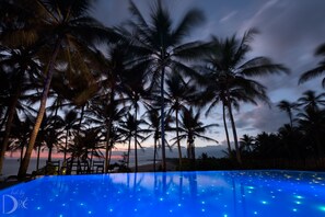 A pool with a blue reflective surface, surrounded by palm trees and a sunset view.