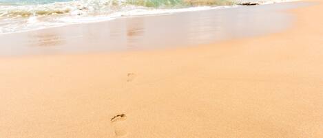 A beach with clear water, a sandy shore, and large rocks.