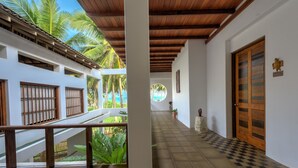 A corridor with a checkered floor, wooden doors, and a view of palm trees outside.