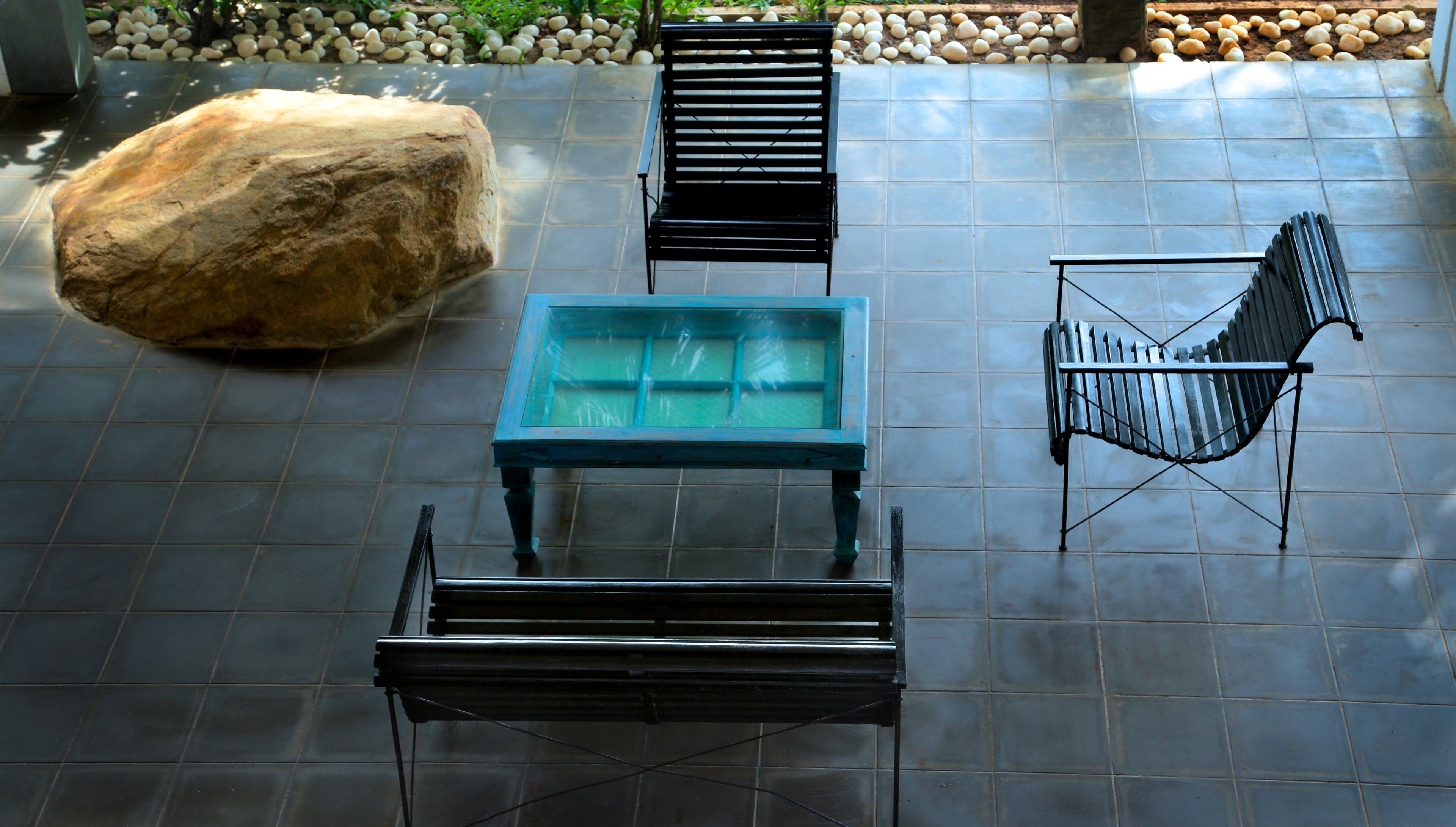 A patio area with a large rock, a teal table, and three black chairs.