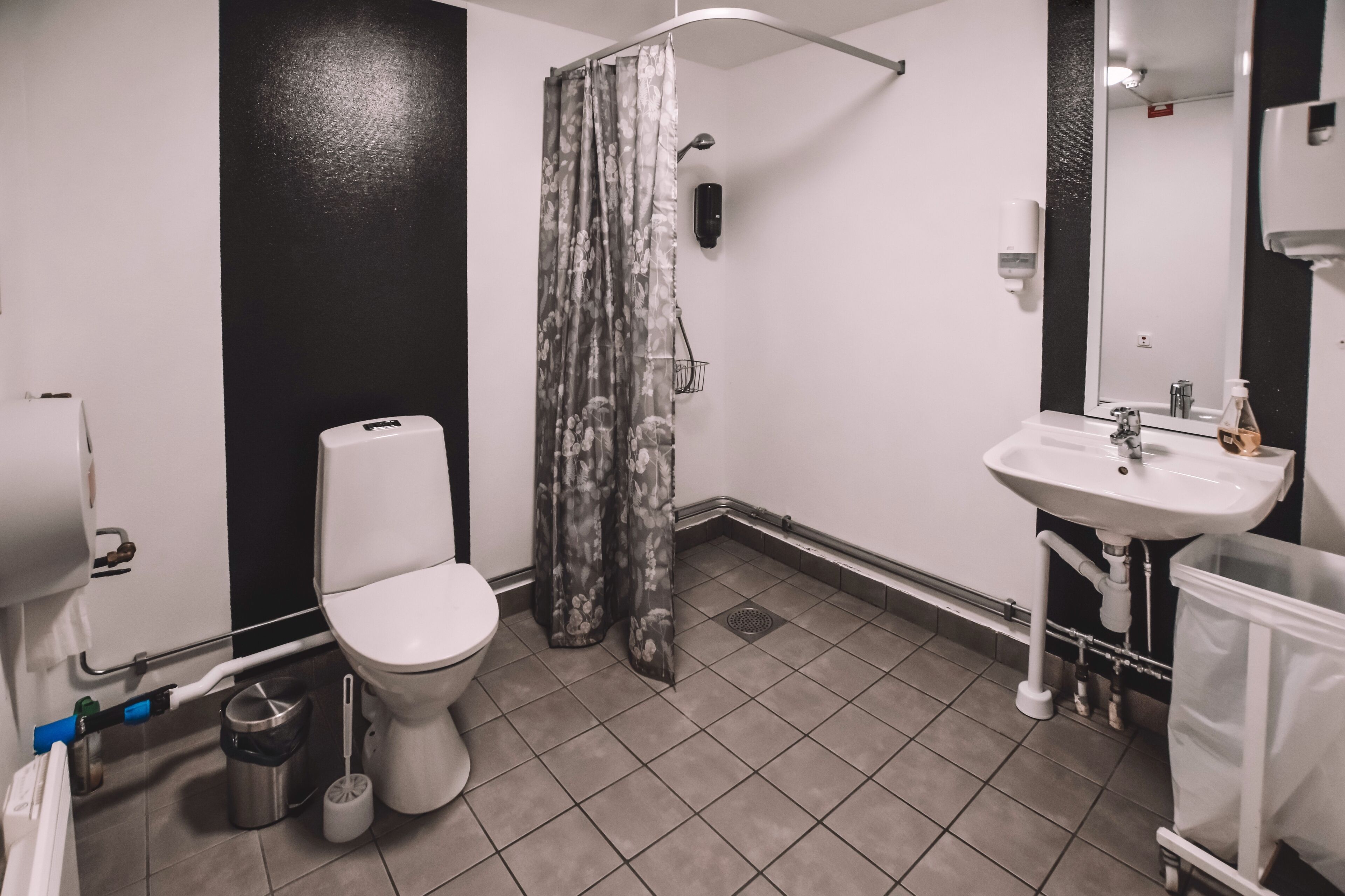 A bathroom with a toilet, shower curtain, sink, and hand dryer.