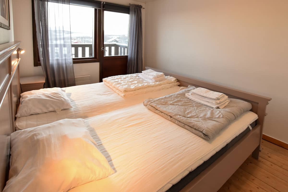Ein Hotelzimmer mit zwei Betten, einem Fenster mit Vorhängen, einem Heizkörper und Blick auf einen Balkon.