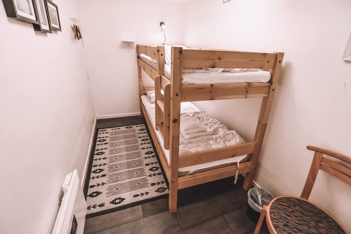 Ein Stockbett mit einem gemusterten Teppich, einem Heizkörper und einem Stuhl.