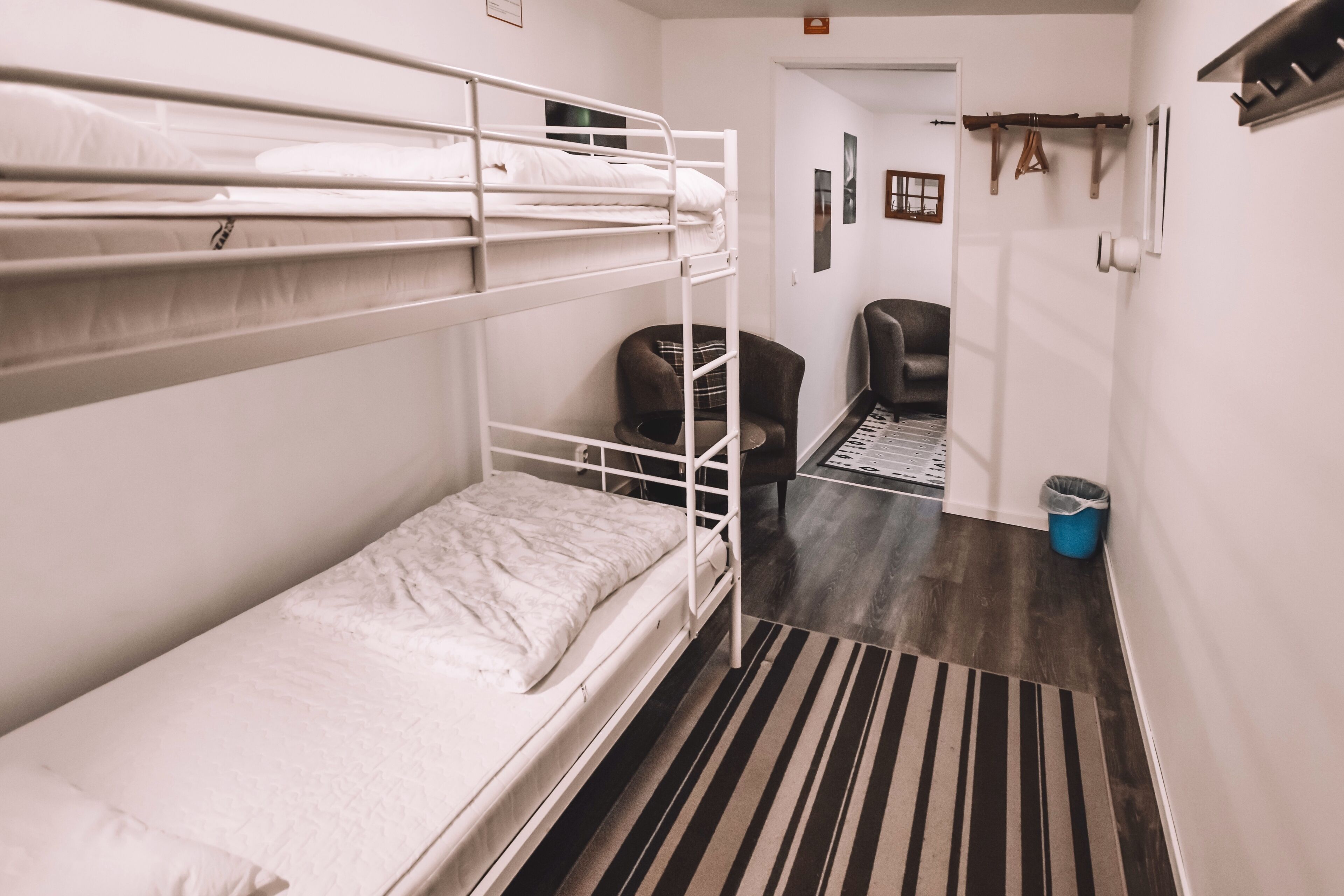Habitación con literas, un tapete a rayas, una silla y un cesto de basura.