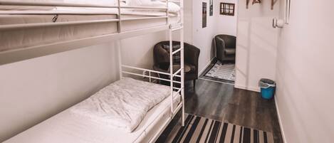 Une chambre avec un lit superposé, un tapis à rayures, une chaise et une poubelle.