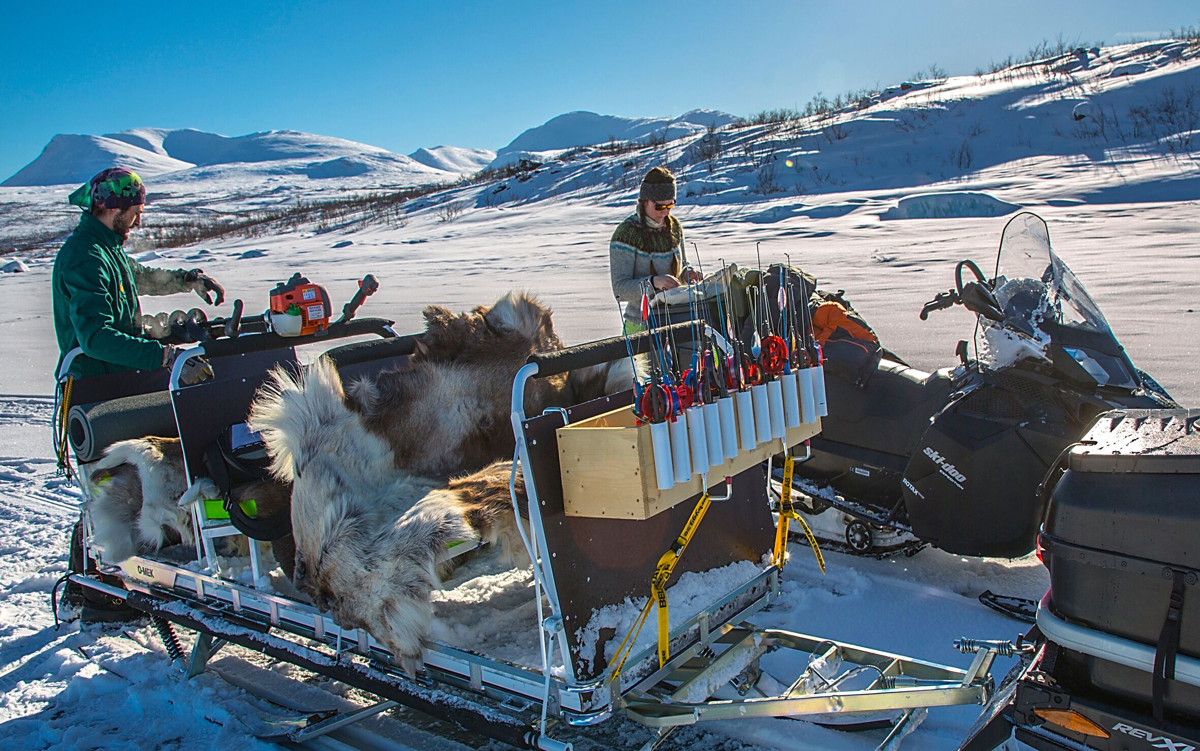 Une motoneige à laquelle est attachée une luge, un chien et une personne portant une veste verte.