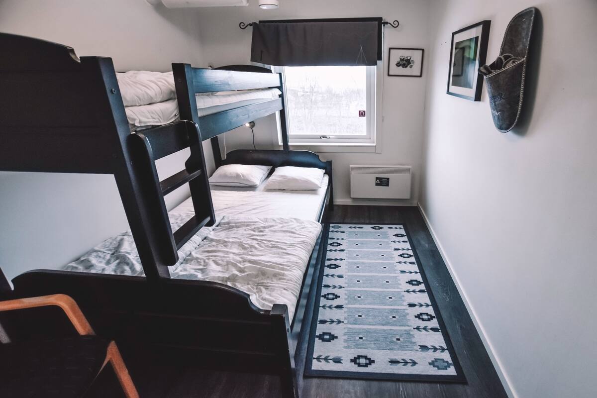Ein Schlafzimmer mit Etagenbetten, einem Fenster, einer Heizung, einem gemusterten Teppich und einem gerahmten Bild an der Wand.