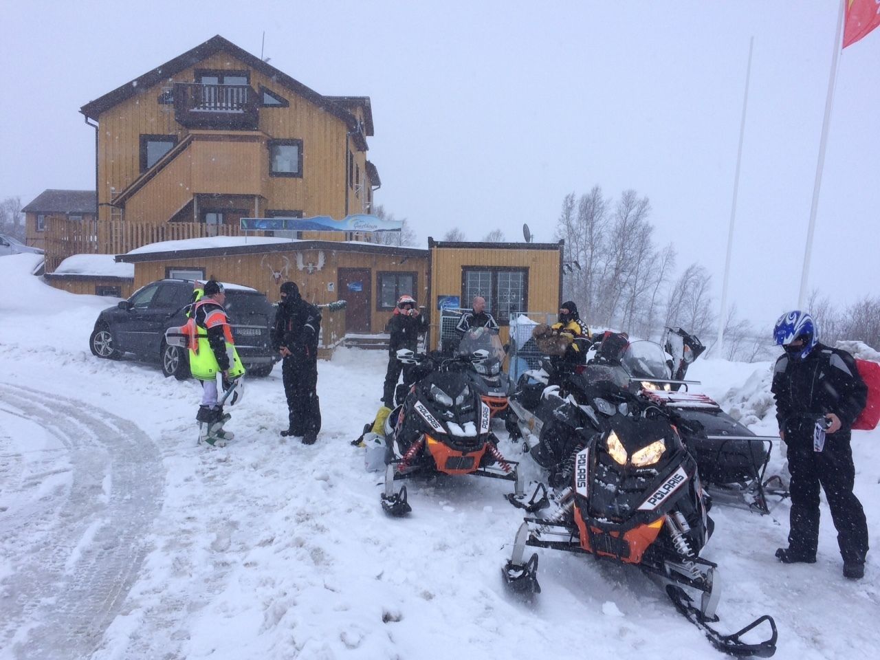 A snow-covered area with a building and parked snowmobiles.