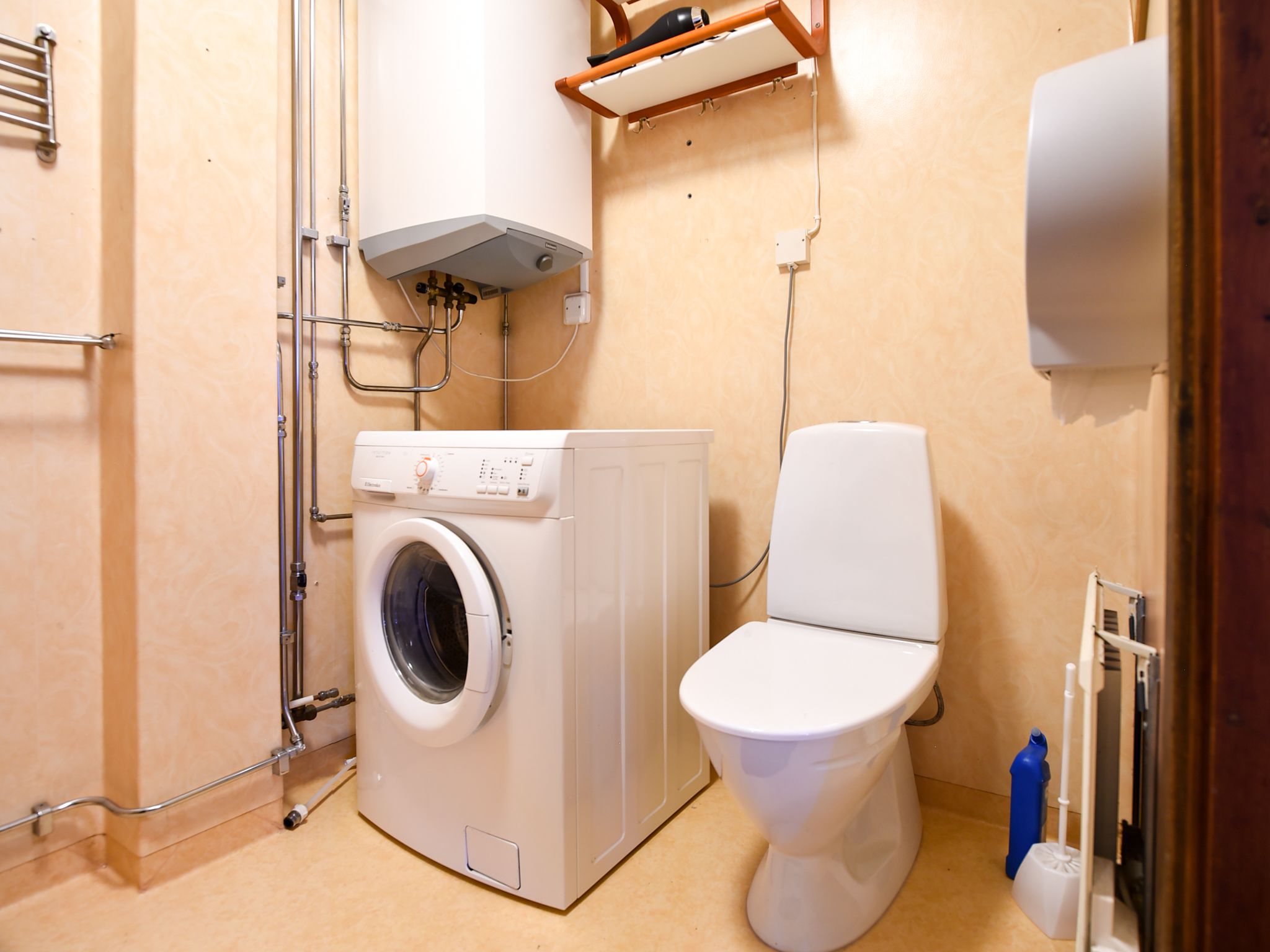 A compact bathroom with a washing machine, toilet, and a small shelf with a hairdryer.