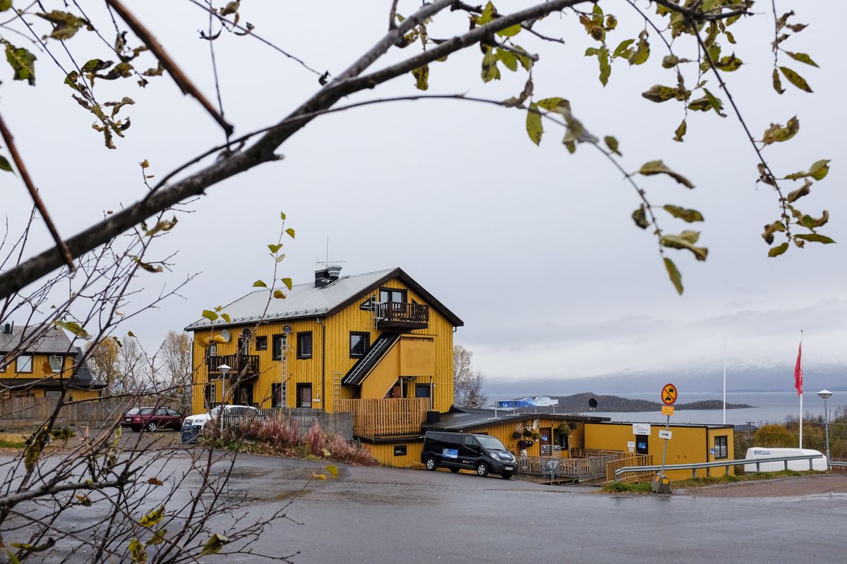 A yellow building with a staircase, a car parked in front, and a no parking sign.