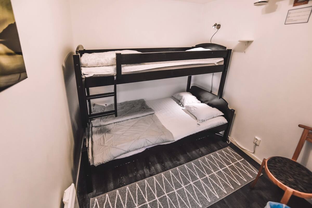 Ein Stockbett mit einem gemusterten Teppich, einem kleinen Tisch und einer Wandlampe.