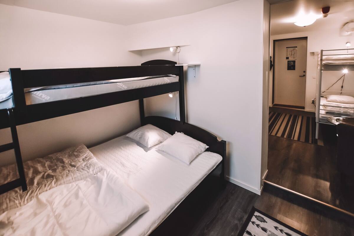 Ein Stockbett mit Schreibtisch und Spiegel, ein Holzboden und eine Tür zu einem anderen Raum.