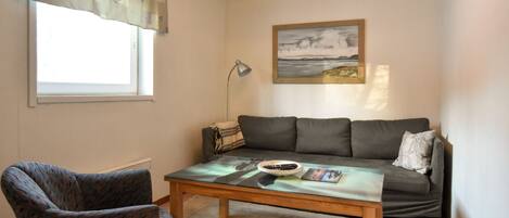 Ein Wohnzimmer mit Sofa, Sessel, Couchtisch und einem Gemälde an der Wand.